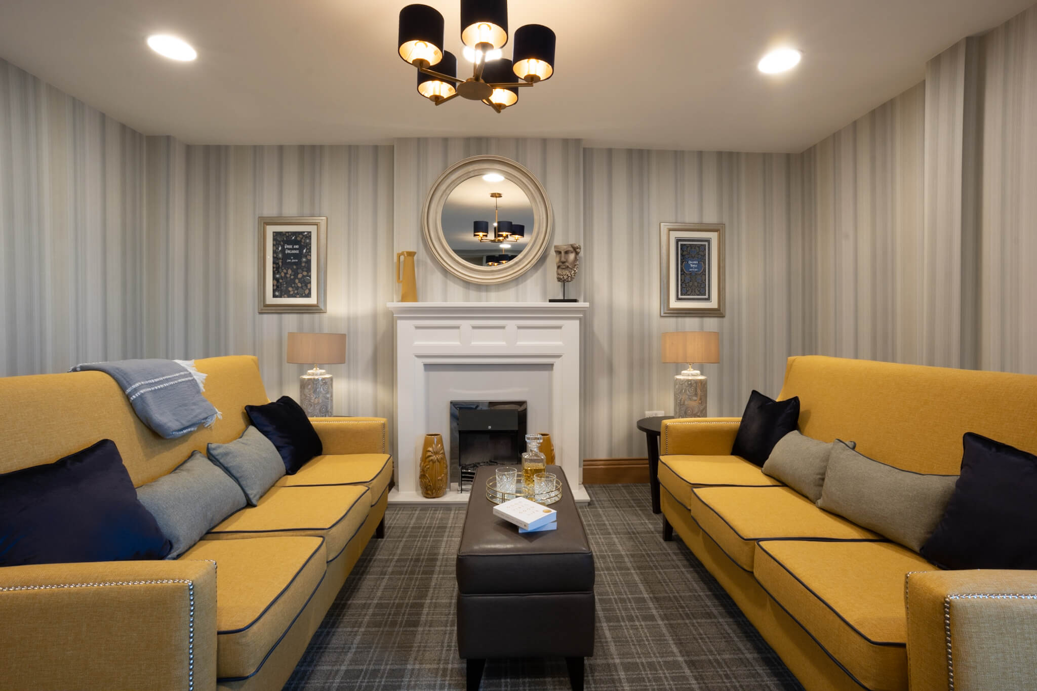 Striped wallpaper. Circle mirror above a fireplace. Mustard sofas. Checked carpet.