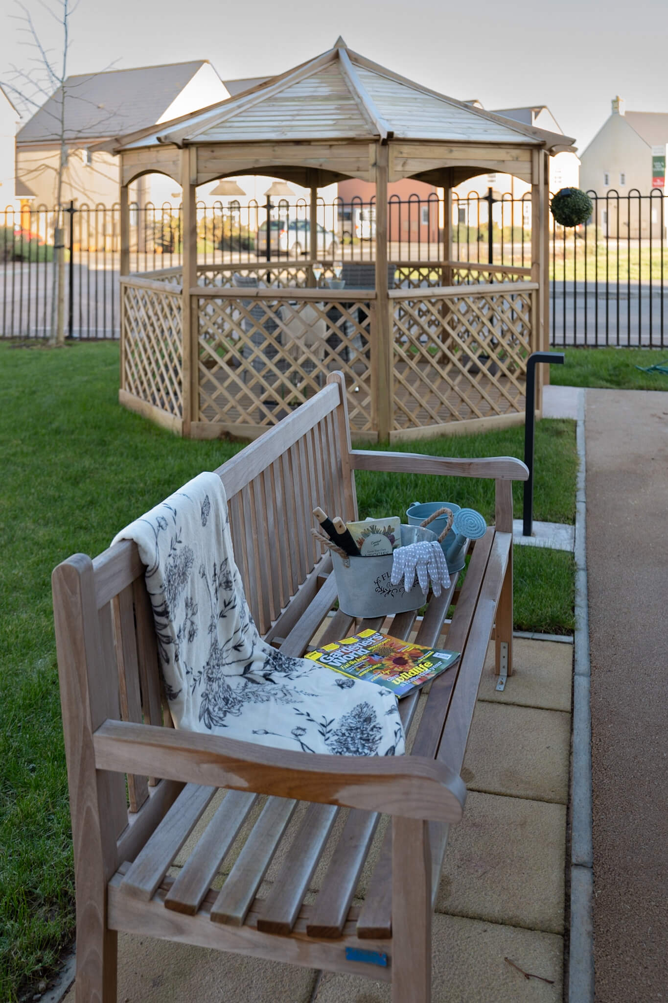 Pergola in background. Garden seating with blanket and gardening tools on top.