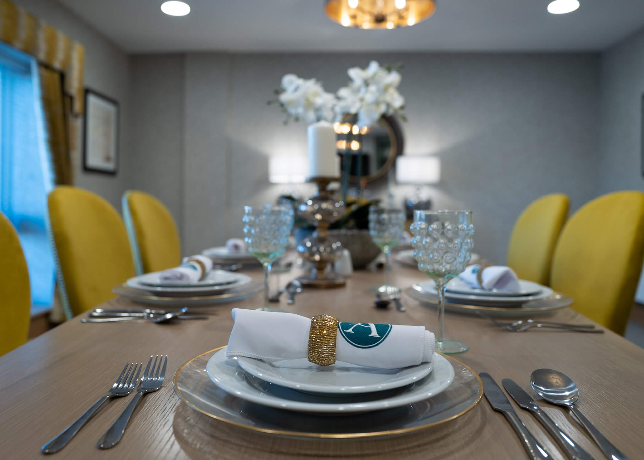 A dressed dining room table with a Alexander House napkin. Yellow dining room chairs.