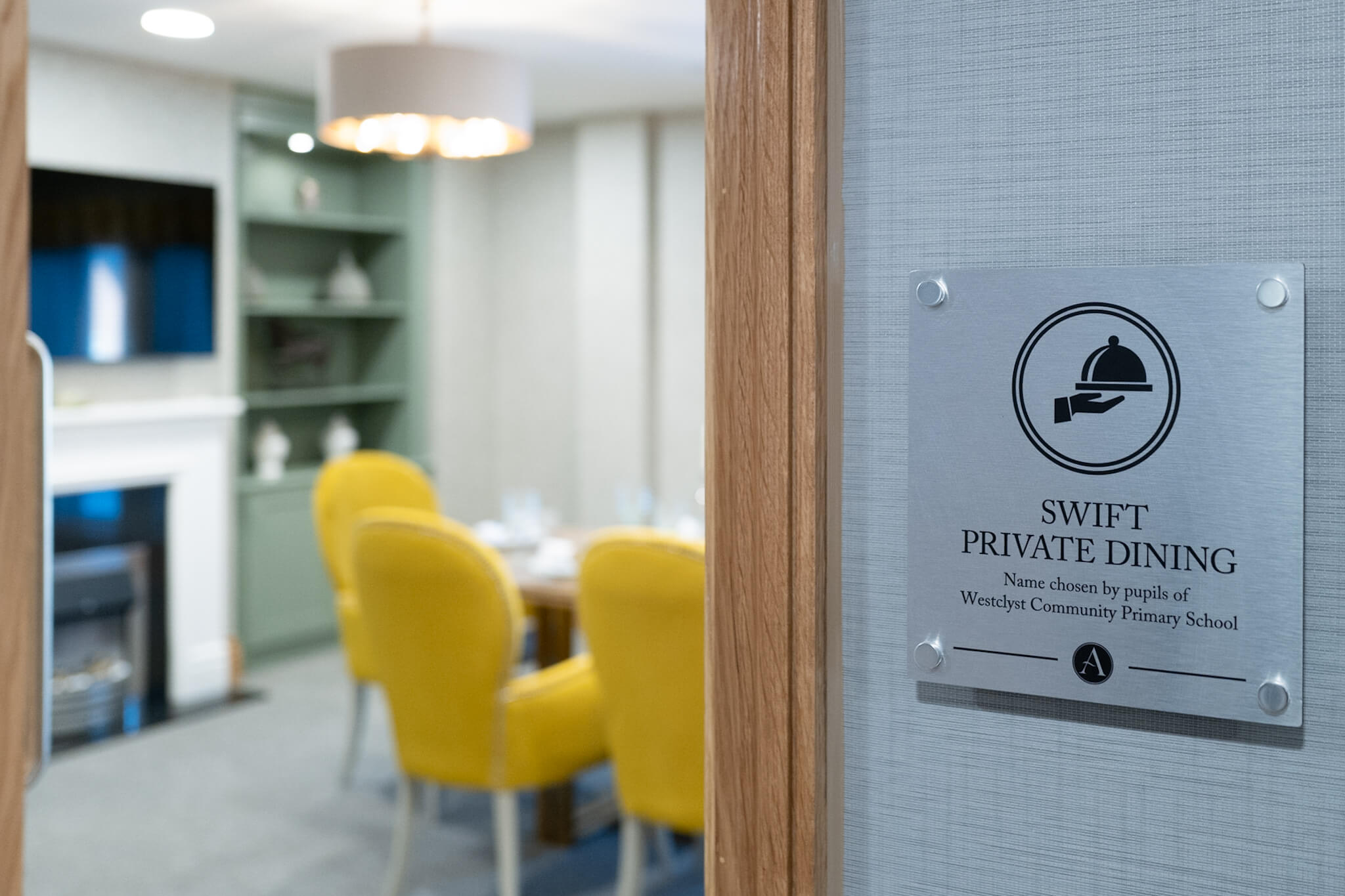 Sign "Swift Private Dining". Blurred image of private dining area. Yellow dining chairs. TV on wall.