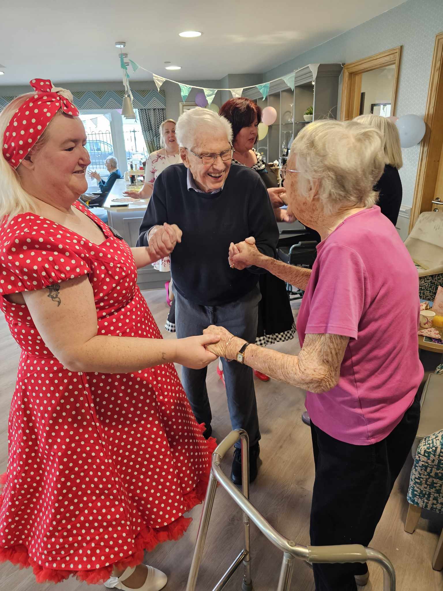 A female dress in a 50's style red dress dancing holding hands with a male and female residents.