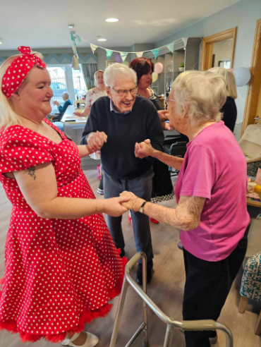 A female dress in a 50's style red dress dancing holding hands with a male and female residents.