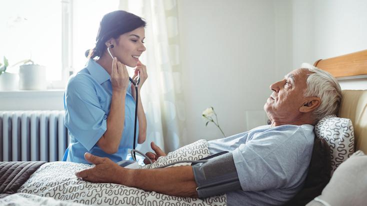 a nurse with a stethoscope tallking to a resident laying in a bed